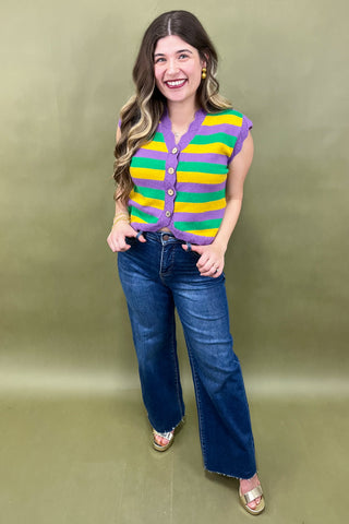 Woman wearing a colorful striped sweater and blue jeans against a green background
