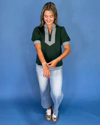 Woman wearing a green top with gray accents and light blue jeans on a blue background