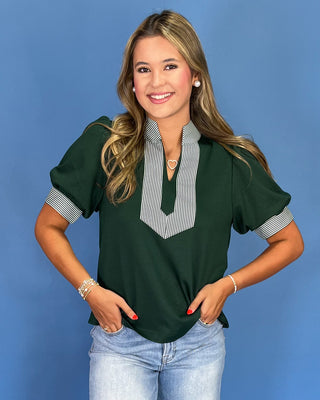 Woman wearing a green blouse with striped collar and blue jeans against a blue background