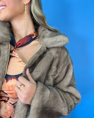 Taupe faux fur cropped jacket with plush texture, oversized collar, long sleeves, and front zipper closure.
