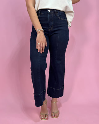 Person wearing dark blue jeans and a white top on a pink background