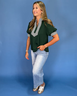 Woman wearing a green top with gray accents and blue jeans on a blue background