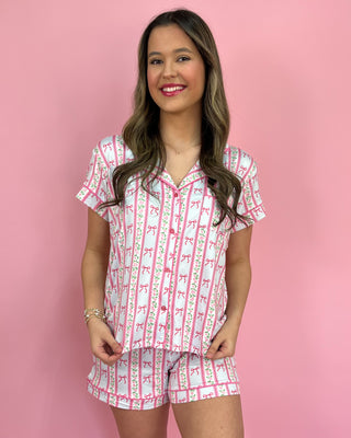 Woman wearing a pink and white patterned pajama set against a pink background