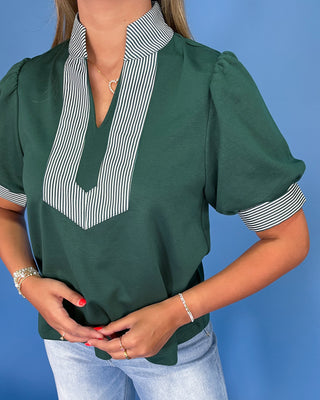 Green blouse with striped collar and cuffs worn by a person on a blue background