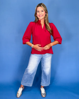 Woman wearing a red blouse and blue jeans against a blue background