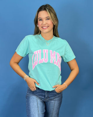 A woman modeling a mint green graphic t-shirt with 'LULU MAC' printed in pink across the chest