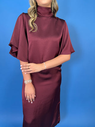 Burgundy satin midi dress with a turtleneck, flutter sleeves, relaxed silhouette, and side slit detail.