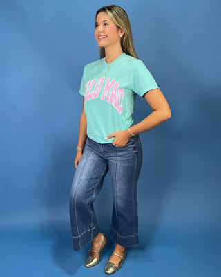 A woman modeling a mint green graphic t-shirt with 'LULU MAC' printed in pink across the chest