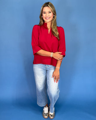 Woman wearing a red blouse and blue jeans against a blue background