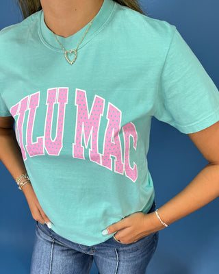 A woman modeling a mint green graphic t-shirt with 'LULU MAC' printed in pink across the chest