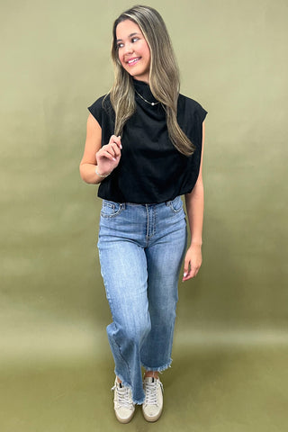 Woman wearing a black sleeveless top and blue jeans against a green background