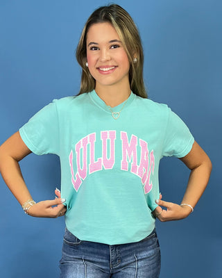 A woman modeling a mint green graphic t-shirt with 'LULU MAC' printed in pink across the chest