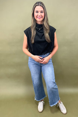 Woman wearing a black sleeveless top and blue jeans against a green background