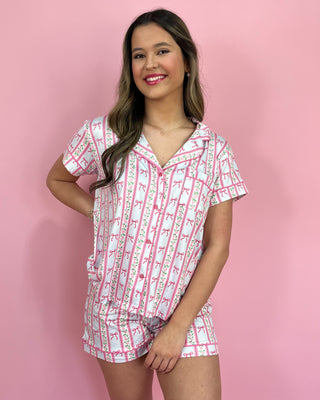 Woman wearing a pink and white patterned pajama set against a pink background
