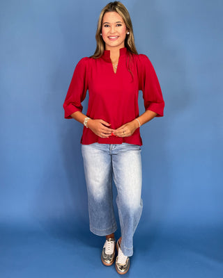 Woman wearing a red blouse and light blue jeans against a blue background