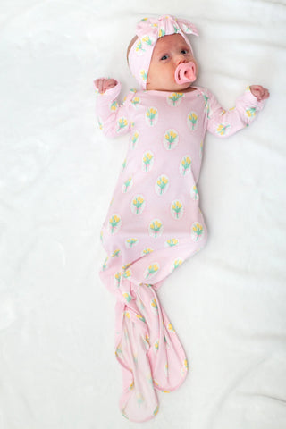 Newborn baby wrapped in a pink floral swaddle with a matching headband on a white background