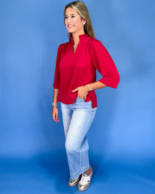 Woman wearing a red blouse and light blue jeans against a blue background