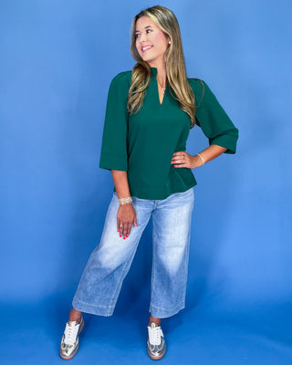Woman wearing a green top and blue jeans against a blue background