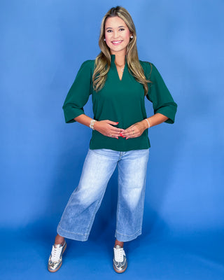 Woman wearing a green top and blue jeans against a blue background