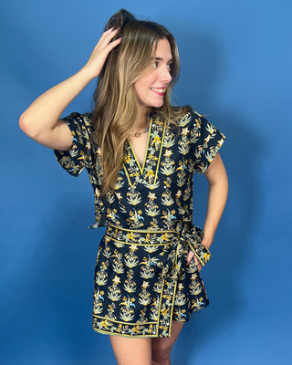 A woman modeling a short-sleeve wrap dress with a navy blue base and a yellow and white floral pattern