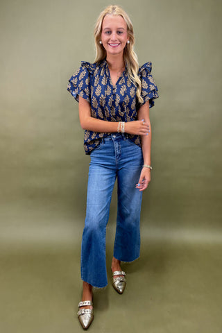 Woman wearing a navy floral blouse and blue jeans against a green background