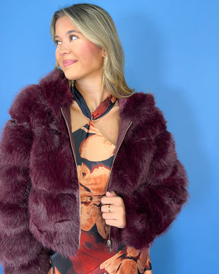 Burgundy faux fur cropped jacket with plush textured fabric, oversized collar, long sleeves, and gold zipper closure.