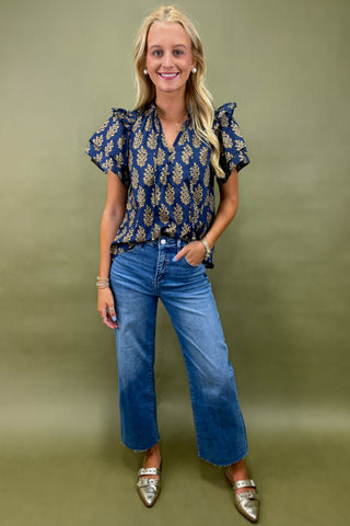 Woman wearing a blue patterned blouse and jeans against a green background