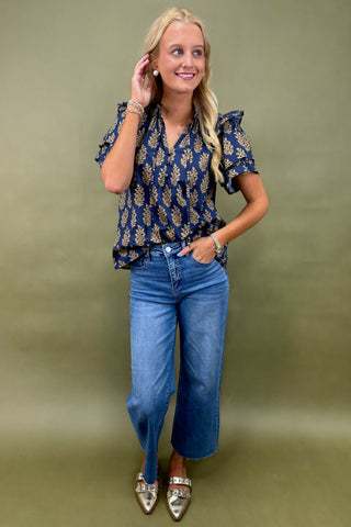 Woman wearing a blue floral blouse and jeans against a green background