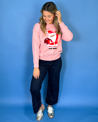 Pink Christmas knit sweater with Santa Claus graphic, white snowflake accents, crew neckline, long sleeves, and ribbed trim.