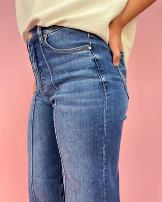 Person wearing blue jeans against a pink background