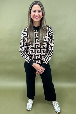 Woman wearing a patterned sweater and black pants on a green background