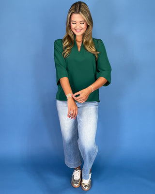 Woman wearing a green top and light blue jeans against a blue background