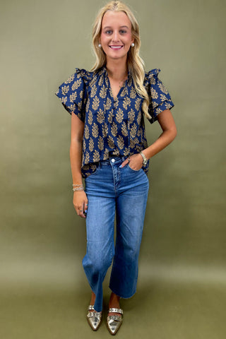Woman wearing a blue patterned blouse and jeans against a green background