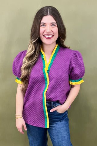 Woman wearing a purple quilted jacket with yellow and green accents against a green background