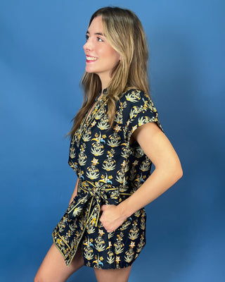 A woman modeling a short-sleeve belted romper with a navy blue and yellow floral pattern