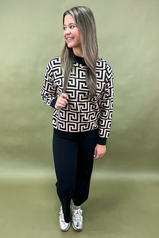 Woman wearing a black and white patterned top with dark pants on a green background