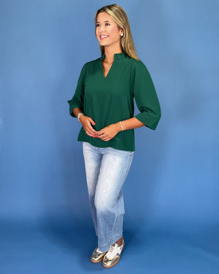 Woman wearing a green top and light blue jeans against a blue background