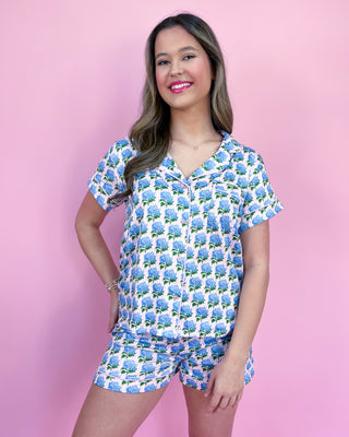 Woman wearing a blue floral pajama set against a pink background