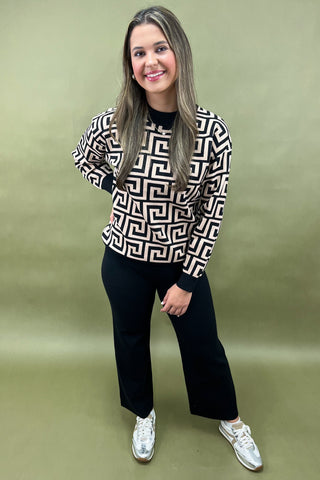 Woman wearing a patterned sweater and black pants against a green background