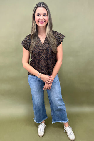 Woman wearing a leopard print top and blue jeans against a plain background