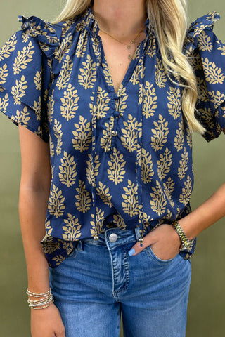 Woman wearing a blue blouse with gold leaf pattern and blue jeans against a green background