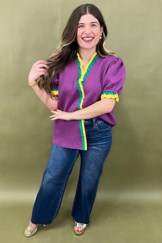 Woman wearing a purple blouse with yellow and green accents and blue jeans against a green background