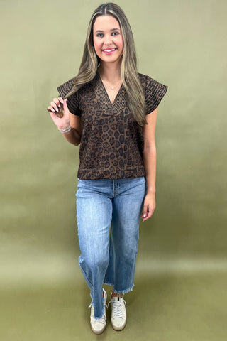 Woman wearing a leopard print top and blue jeans against a plain background