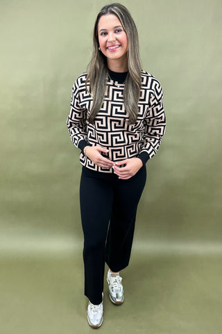 Woman wearing a patterned sweater and black pants on a green background
