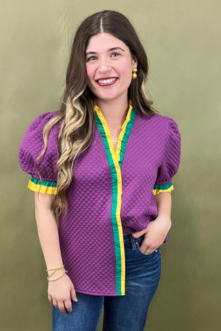 Woman wearing a purple textured top with yellow and green trim against a green background
