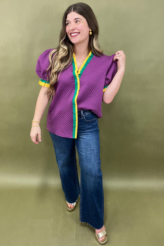 Woman wearing a purple blouse with yellow accents and blue jeans against a green background