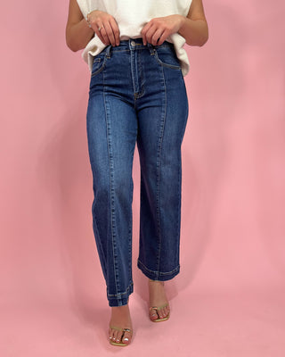Person wearing blue jeans against a pink background