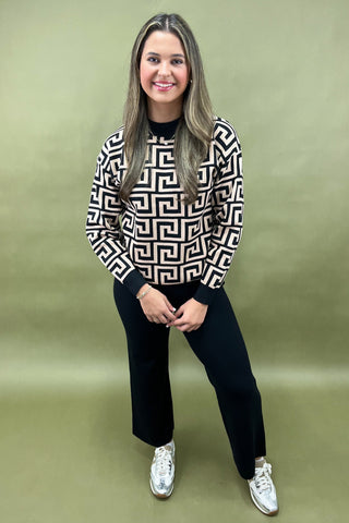 Woman wearing a patterned sweater and black pants against a green background