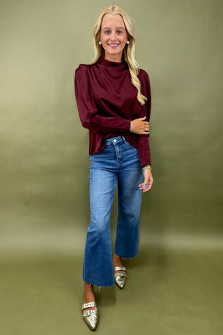 Woman wearing a burgundy top and blue jeans against a green background