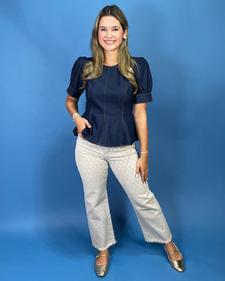 A woman modeling a navy blue short-sleeve peplum top with puff sleeves, paired with light gray patterned jeans and metallic gold flats